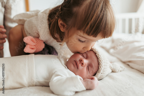 Toddler sister giving a gentle kiss to her sleeping newborn brother