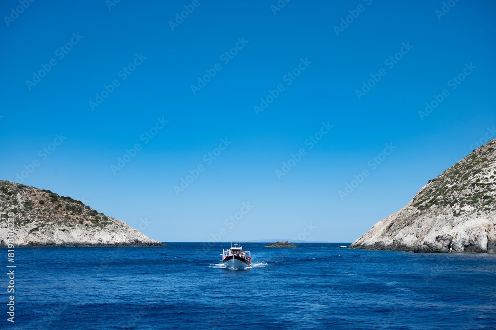 Small vessel is seen sailing in a tranquil lake surrounded by mountain peaks, Greece, Zakynthos Small vessel is seen sailing in a tranquil lake surrounded by mountain peaks, Greece, Zakynthos