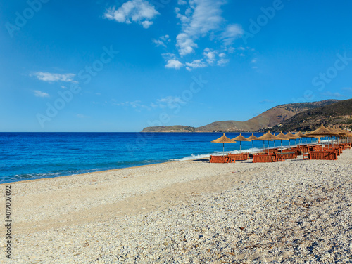 Summer morning pebbly beach with sunbeds and strawy sunshades (Borsh, Albania).