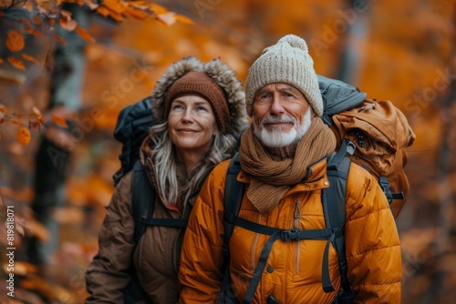 A smiling middle-aged couple in warm clothing poses while hiking in a beautiful autumn forest