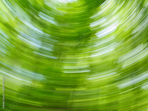 A dynamic, blurred swirl effect of green leaves in a forest capturing motion on a sunny day. © Topuria Design