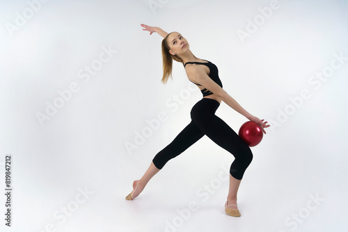 young gymnast in a photo studio shows the elements of exercises with a ball © Alex