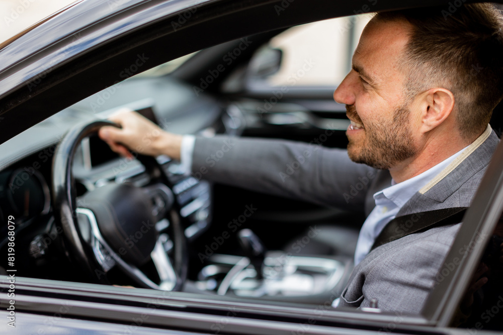 Smiling businessman driving luxurious car through city streets on a sunny day