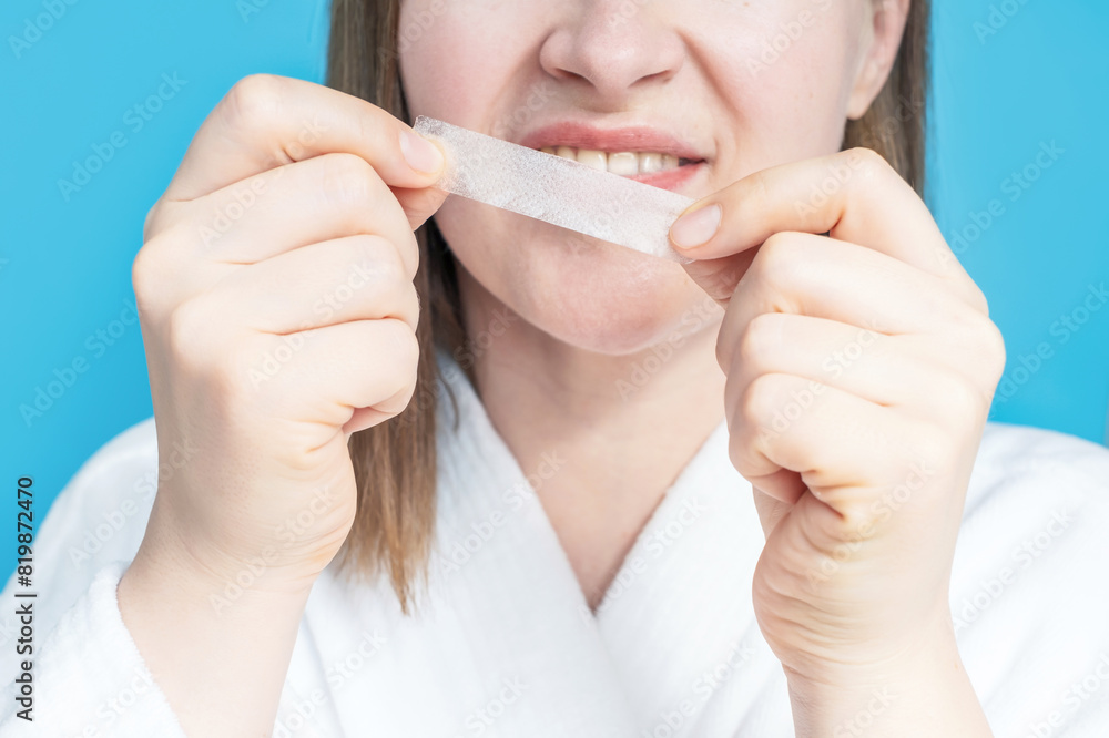 Portrait of a young woman holding a whitening strip for teeth, close-up. Portrait of a young woman holding a whitening strip for teeth, close-up.