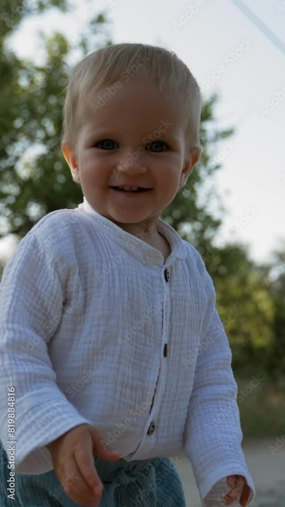 Cute toddler walks on road turning head and looking at camera. Cheerful little boy spends summer vacation in countryside close view slow motion Vertical Shot. Cute toddler walks on road turning head and looking at camera. Cheerful little boy spends summer vacation in countryside close view slow motion Vertical Shot.