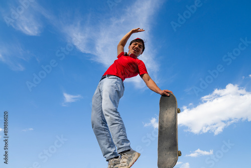 young man posing happy with skateboard in hand background blue and cloudy. youth sports and entertainment concept