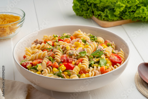 Homemade macaroni salad with trivelle pasta and canned tuna, carrot, Head Lettuce, tomato, corn and mayonnaise dressing in a white plate on wooden table. photo