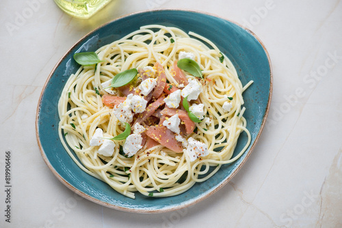 Turquoise plate with smoked salmon and feta spaghetti, horizontal shot on a beige granite background, elevated view