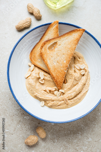 Blue and white plate with peanut butter and toasts, vertical shot on a beige stone background, high angle view