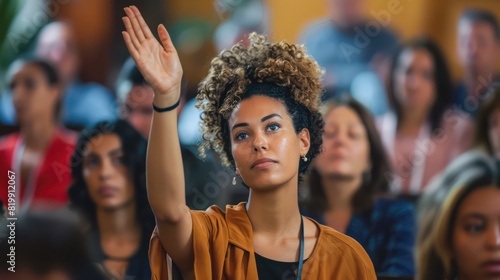 A female entrepreneur stands out in the audience, her hand raised high as she prepares to contribute her perspective during a conference.