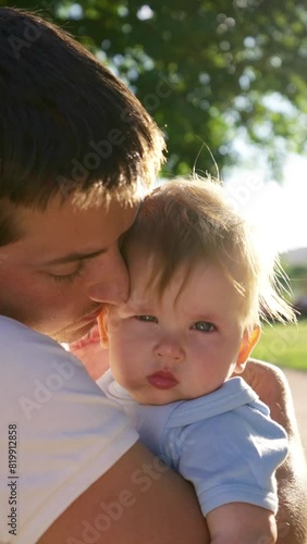 Father plays with concerned baby girl hugging in arms. Stylish father strokes baby daughter and calms down. Man wearing white t-shirt looks happy closeup Vertical Shot.