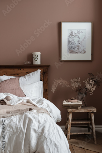 A bedroom wall is painted in a dusty rose color  the bed is made with white linen and has an old wooden headboard  and there is some framed art on one of the walls.