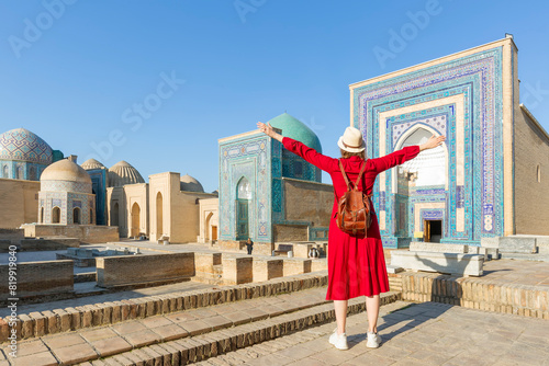 Young tourist dressed in red with arms raised in front of the Shah-I-Zinda memorial complex in Samarkand, Uzbekistan. photo