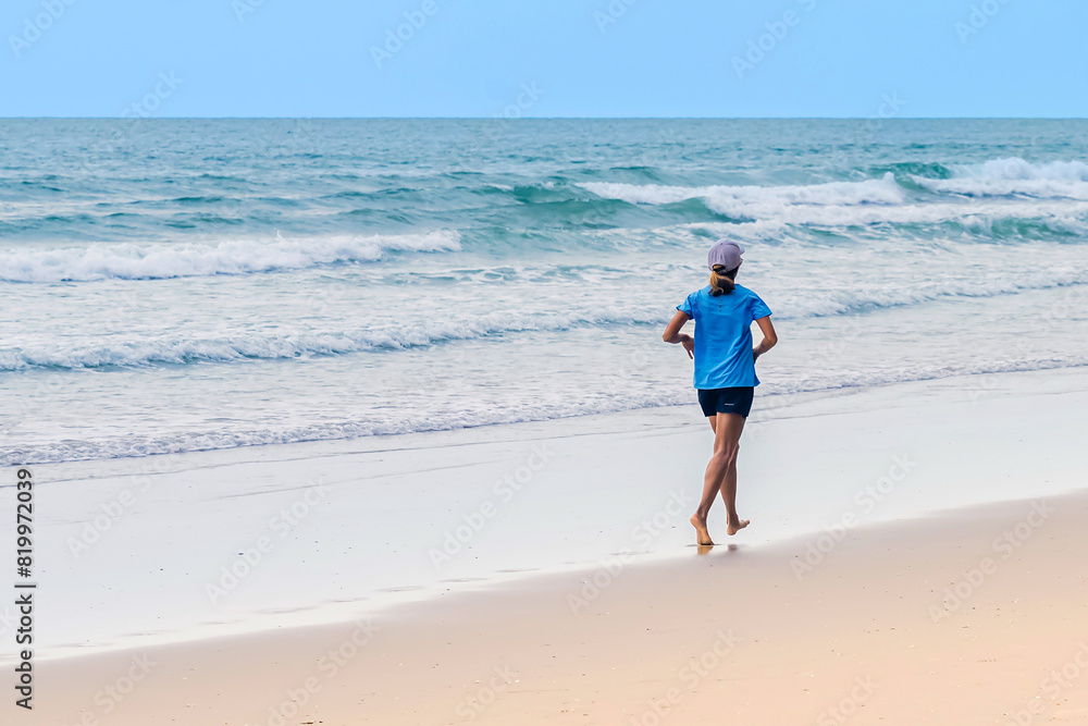 Fit young woman running on beach. Active and Happy woman in active sportswear with hat enjoy jogging on beach in the morning. Fitness girl with summer sport and freedom, exercise and healthy concept.