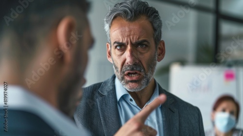 Man in suit with gray hair and beard pointing finger at another man engaged in a serious conversation.