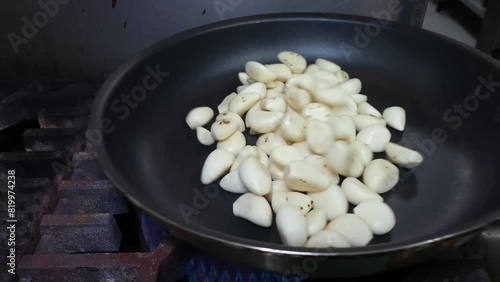 Peeled garlic cloves are being sautéed in a dry non-stick pan, turning golden brown with char marks.