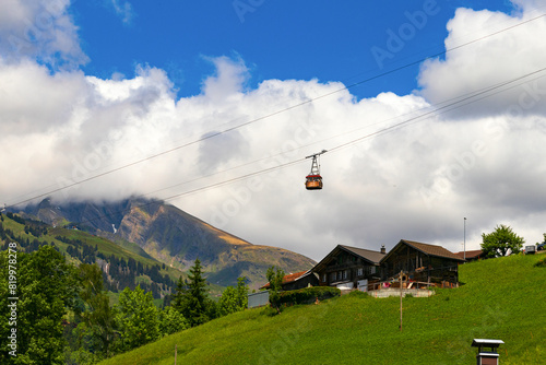 A picturesque panoramic view of the green slopes of the village of Grindelwald and the old cable car with a cabin on the background of a cloudy sky