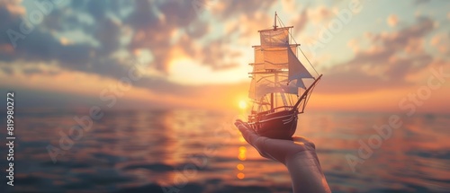 A human hand holding a ship on a vast ocean with a sunset, evoking a sense of exploration with a blurred backdrop #819980272