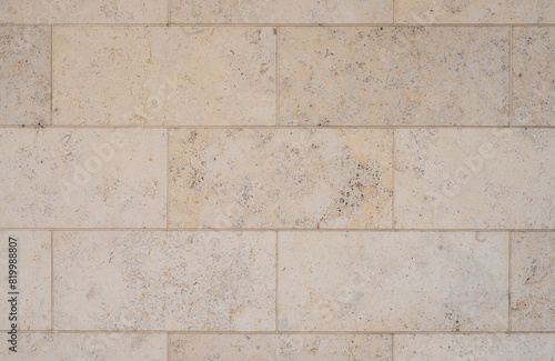 texture of a tiled beige stone wall as background, natural stone wall texture as background. Close-up of a wall clad in limestone