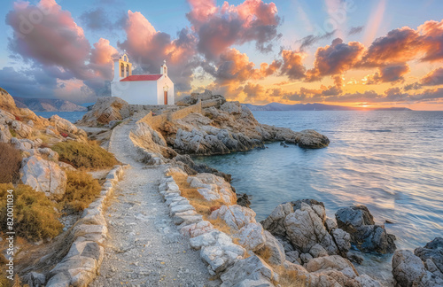 A picturesque scene depicts a small island in Greece, sinister in shape and surrounded by crystal clear waters at sunset. The white chapel stands tall atop it with its red roof standing out against th