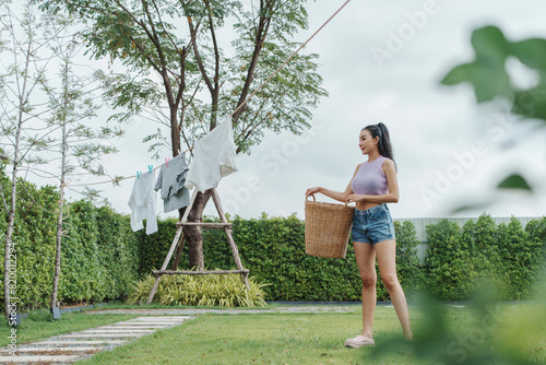 Asian Woman hanging clothes on a clothesline in a sunny backyard, demonstrating a daily chore with a serene and peaceful atmosphere.
