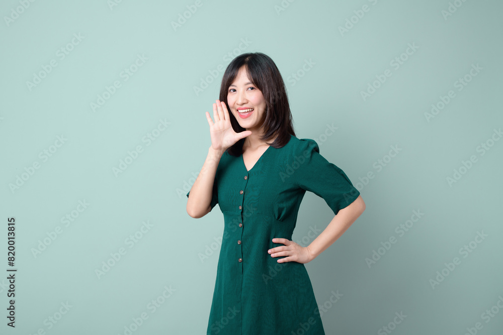 Happy Asian woman shouting above green dress poses against green background blank copy space for advertising content promotion Happy Asian woman shouting above green dress poses against green background blank copy space for advertising content promotion
