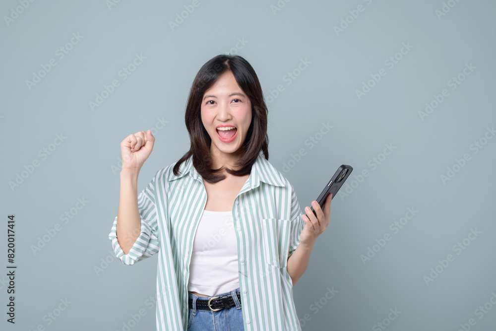 Happy asian woman do winner dance, triumphing, winning on mobile phone video game, holding smartphone horizontal position and celebrating, green background Happy asian woman do winner dance, triumphing, winning on mobile phone video game, holding smartphone horizontal position and celebrating, green background