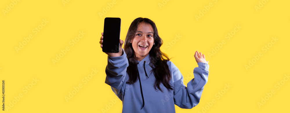 lifestyle: young latina on yellow background shows her smartphone screen with great emotion lifestyle: young latina on yellow background shows her smartphone screen with great emotion