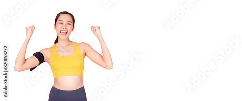 A cheerful young woman in a yellow sports bra and black workout pants celebrating her fitness achievement. She has a smartphone armband and is smiling brightly, exuding energy and motivation against a