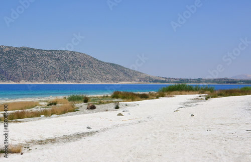 a white sandy beach with blue sea water and a hill in the background