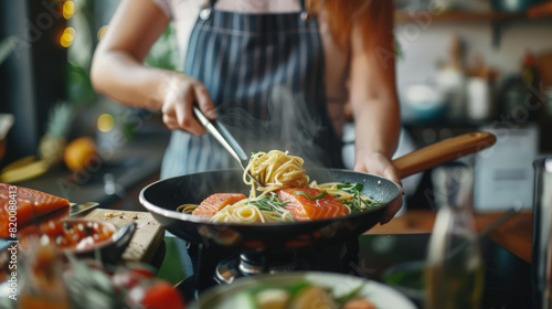 Asian woman hand cooking healthy food pasta and salmon steak on cooking pan in the kitchen at home. Attractive girl preparing food for dinner party celebration meeting with friends on holiday vacation