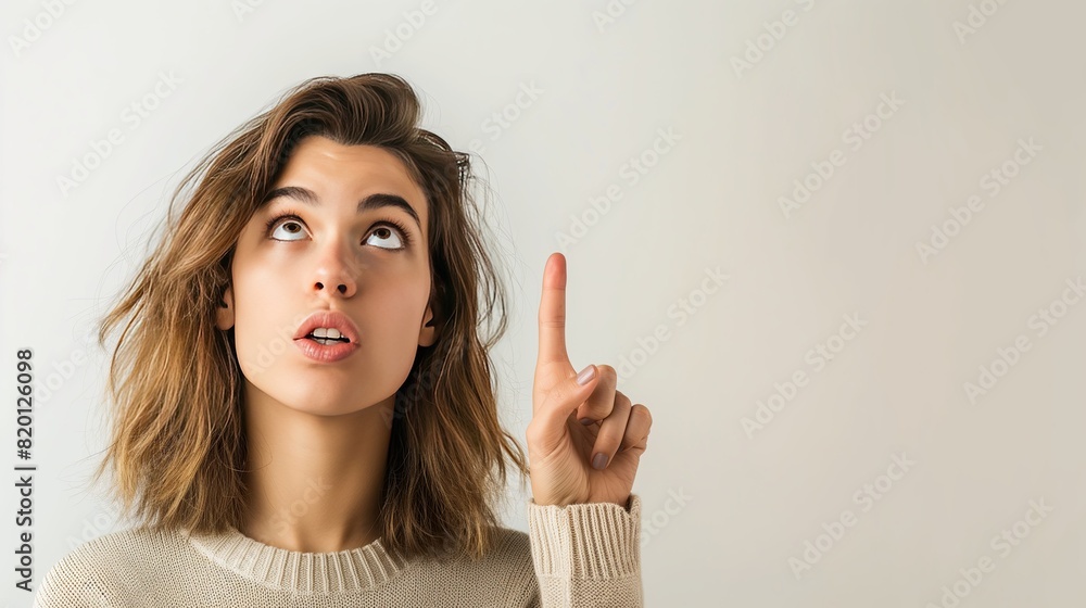 A young woman with an expressive surprised look, wearing a yellow sweater and pointing upward, standing against a plain background.. A young woman with an expressive surprised look, wearing a yellow sweater and pointing upward, standing against a plain background..