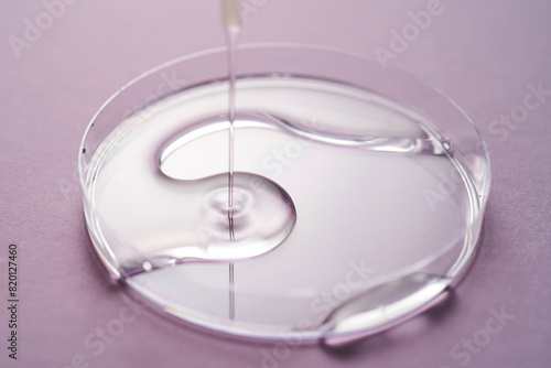 Serum or cosmetic oil flows into a transparent bowl on a purple background.