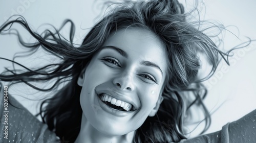A joyful woman is caught in black and white, laughing with windswept hair, showcasing happiness and freedom in a dynamic and expressive manner, reflecting a positive and carefree spirit