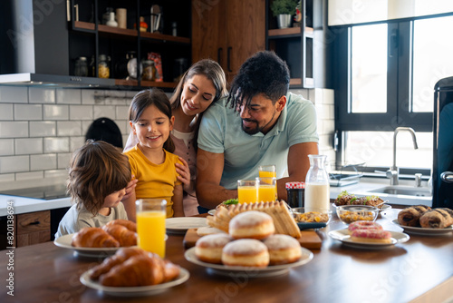 Fotografie Happy parents spending quality time in the morning during weekend having breakfast with children, small lovely boy and girl in the kitchen