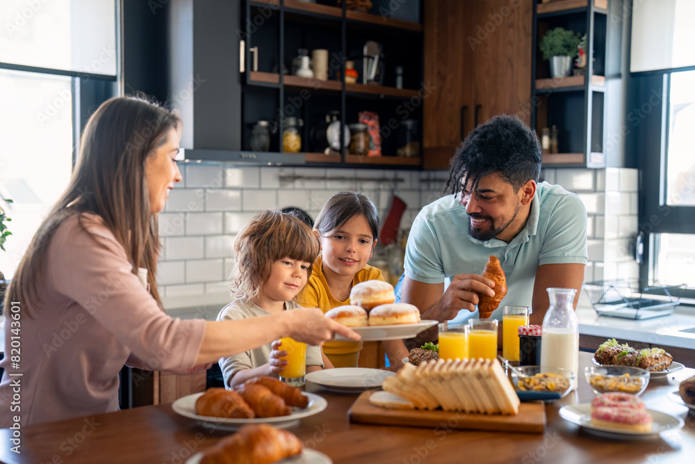 Kids at breakfast with parents. Mother is serving donuts on a plate. Cheerful family moments at home. Kids at breakfast with parents. Mother is serving donuts on a plate. Cheerful family moments at home.