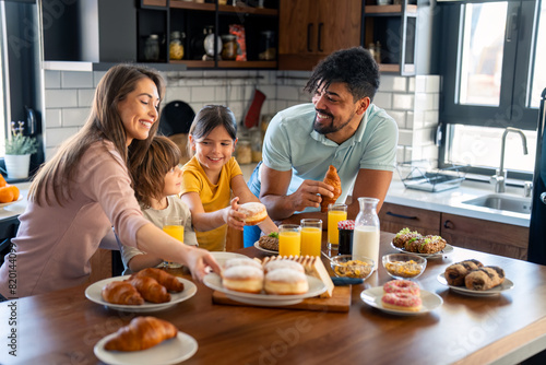 Kids at breakfast with parents. Mother is serving donuts on a plate. Cheerful family moments at home.