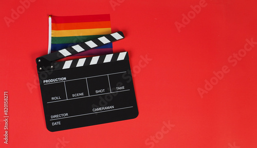 Clapper board and rainbow pride flag on red background.
