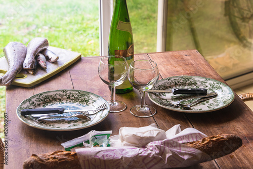 Table setting for dinner or lunch: two plates, forks, knives, glasses, bread on a wooden table