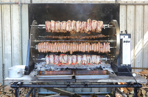 gigantic rotisserie with skewers of meat and sausage that rotates on the burning embers during the village festival photo