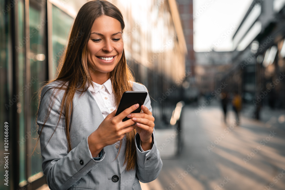 Fototapeta premium Smiling businesswoman using a mobile phone against a city background.