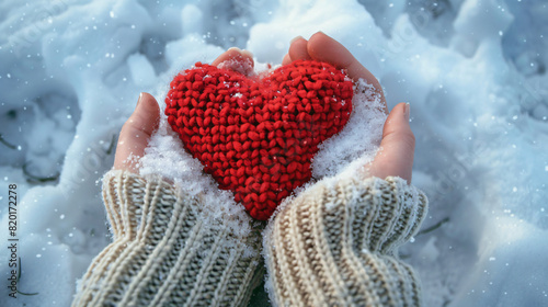 Hands holding red knitted heart in snow