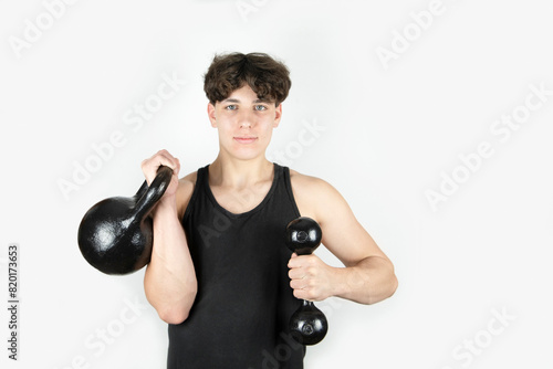 Young self-confident guy likes to do sports for health, guy lifts a heavy kettlebell and holds a heavy dumbbell in other hand. A guy likes to be strong