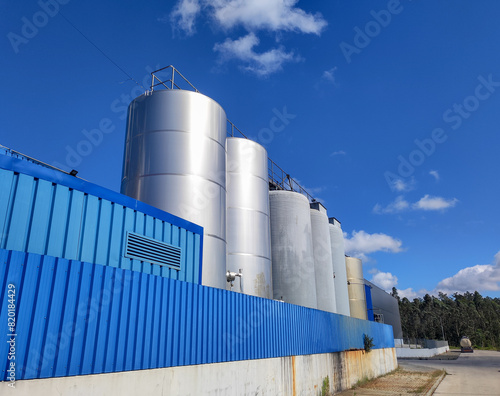 Industrial facility with large storage tanks and blue corrugated metal fence on a clear day in central Portugal