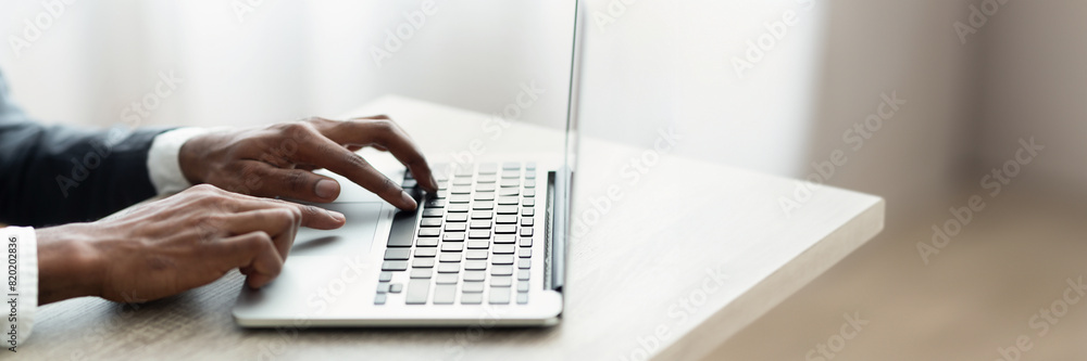 Cropped of african american man in suit typing on laptop keyboard, entrepreneur sending emails, office interior, panorama with copy space Cropped of african american man in suit typing on laptop keyboard, entrepreneur sending emails, office interior, panorama with copy space