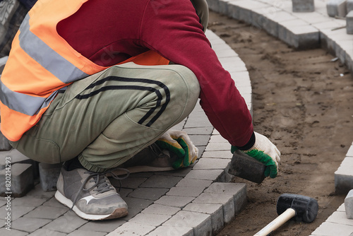 worker wearing gloves uses rubber hammer to lay paving slabs on the street