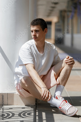 portrait of a young fashionable man in T-shirt, summer shorts and sneakers sitting on staircase on the street, fashionable man, LGBT community