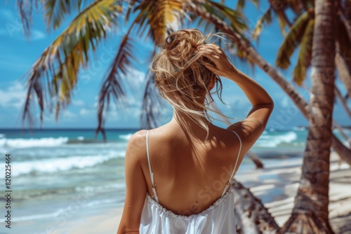 A woman in a white dress on a beach under a palm tree © Aleks