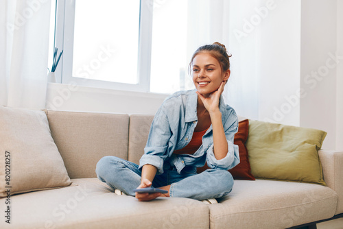 Happy woman holding mobile phone and enjoying online game on cozy sofa in living room