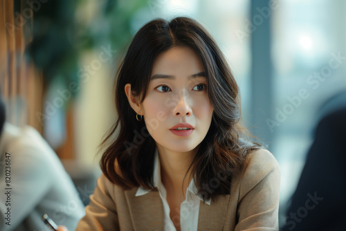 A young Asian businesswoman with a contemplative expression sits in an office 